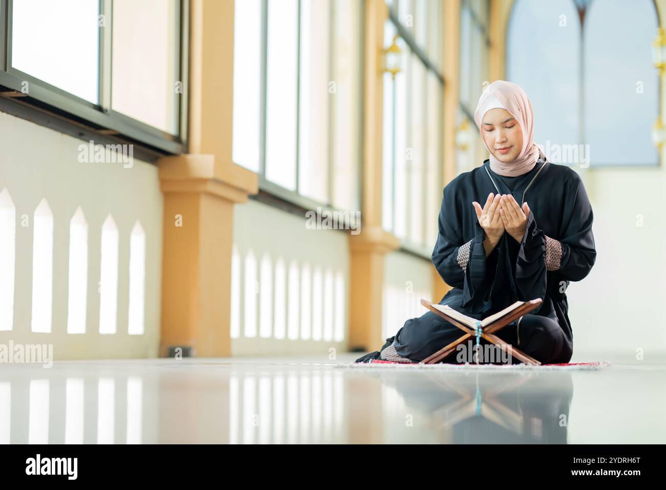 L'immagine di una donna musulmana asiatica nella religione islamica in hijab di colore crema. Leggere il Corano e avere una faccia felice sorridente alloggiando in un bea Foto Stock