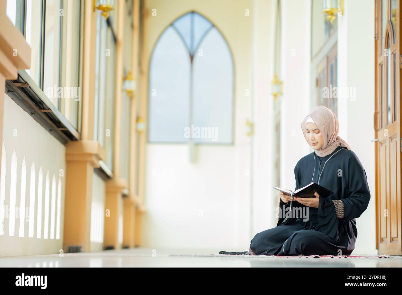 L'immagine di una donna musulmana asiatica nella religione islamica in hijab di colore crema. Leggere il Corano e avere una faccia felice sorridente alloggiando in un bea Foto Stock