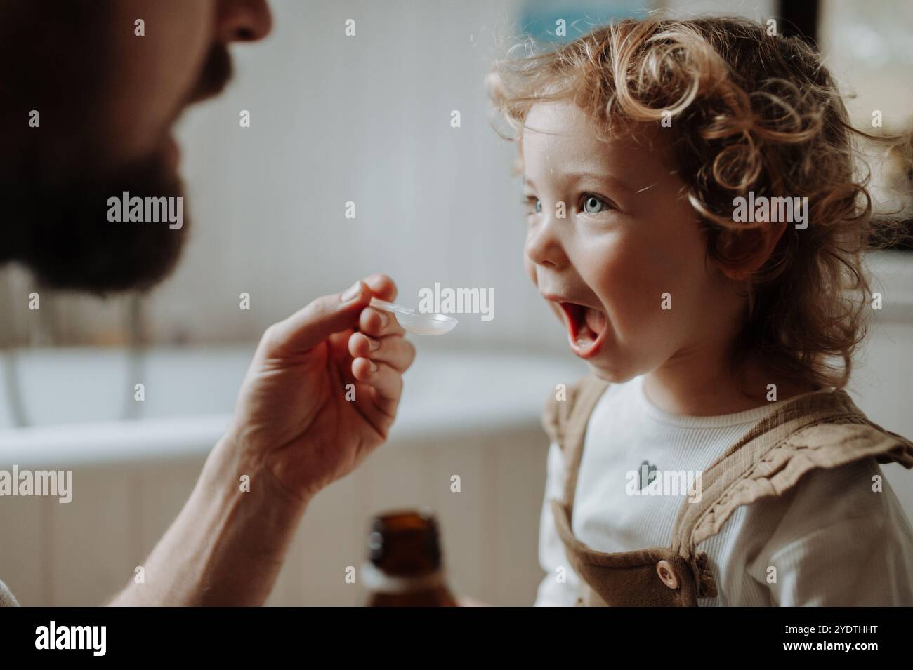 Ragazza malata con febbre e freddo a casa. Padre che dava alla figlia medicine su cucchiaio, sciroppo per tosse o medicina per la febbre. Foto Stock