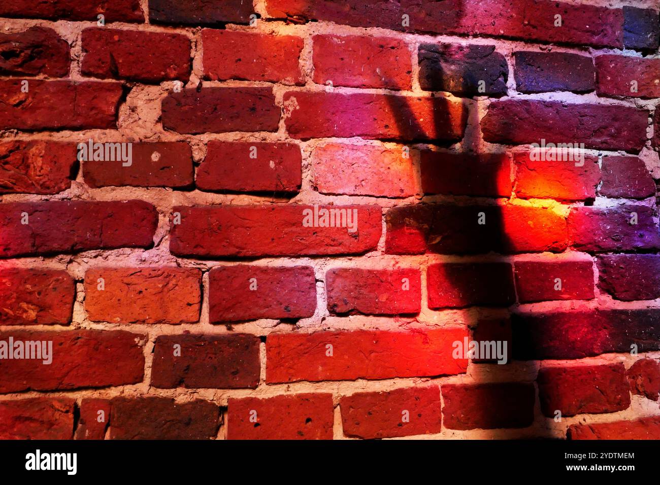 Un muro di mattoni rossi con riflessi rossi da una finestra di vetro colorato. L'ombra di un braccio allungato con le dita spalmate Foto Stock