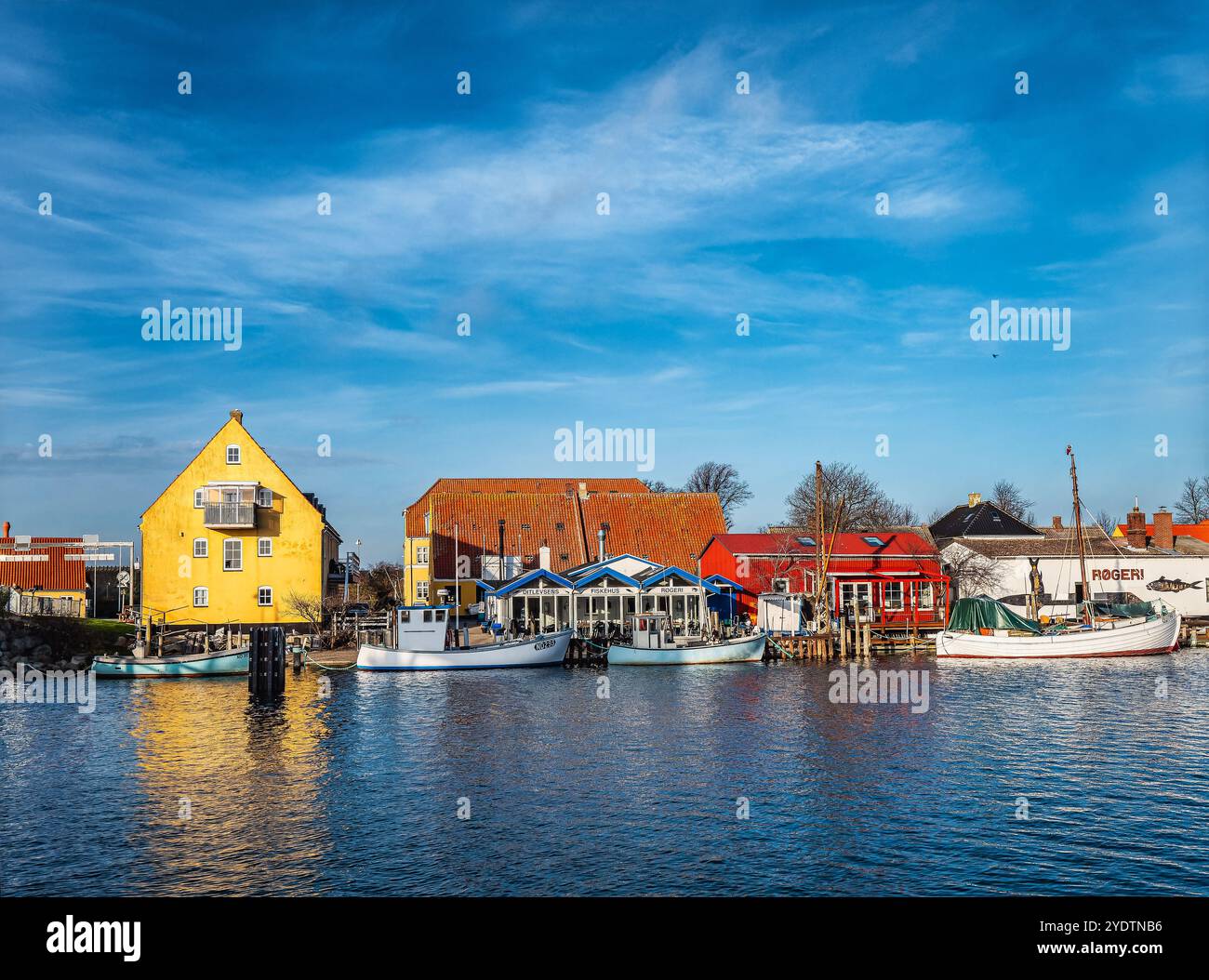 Pittoresco villaggio costiero di Karrebaeksminde, con vivaci case gialle e rosse, tradizionali barche da pesca e un mare blu calmo sotto un chiaro sk Foto Stock