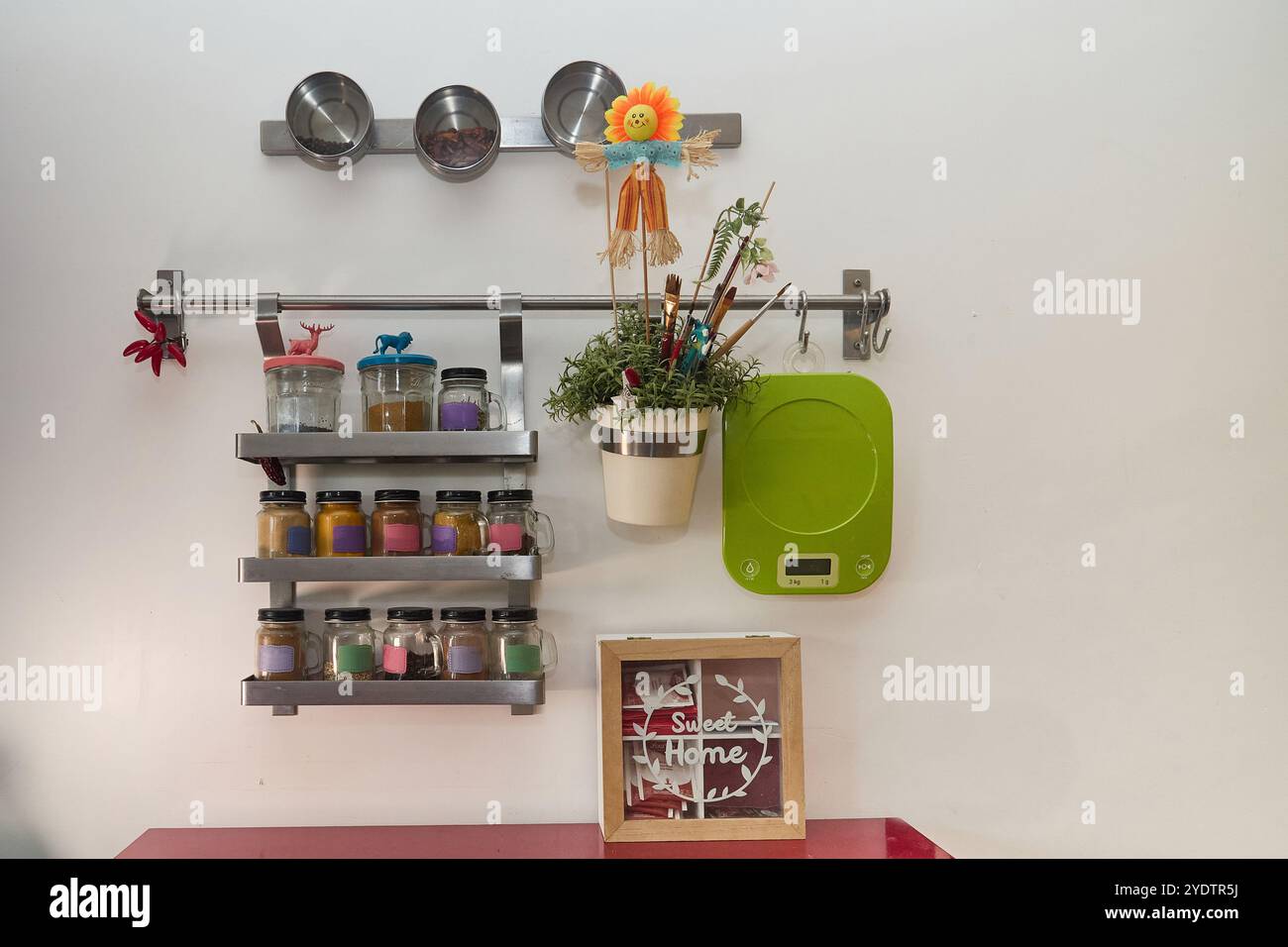 Parete portaspezie in una cucina moderna con molti contenitori colorati, una bilancia elettronica, una pentola con piante e una vasta gamma di altri arredi da cucina Foto Stock