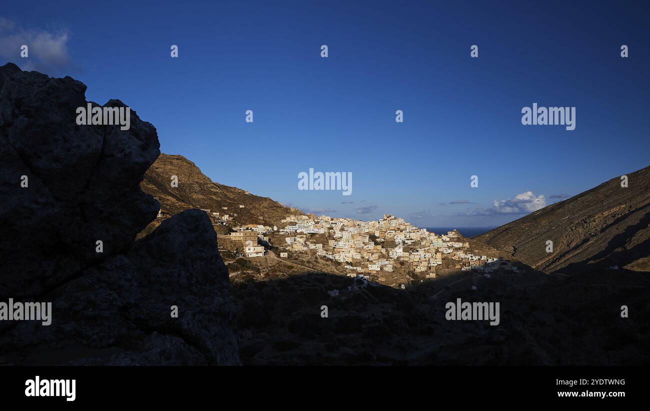 Un villaggio alla luce del mattino presto, circondato da colline e rocce scure, illuminato da luna o stelle, colorato villaggio di montagna, luce mattutina, Oly Foto Stock