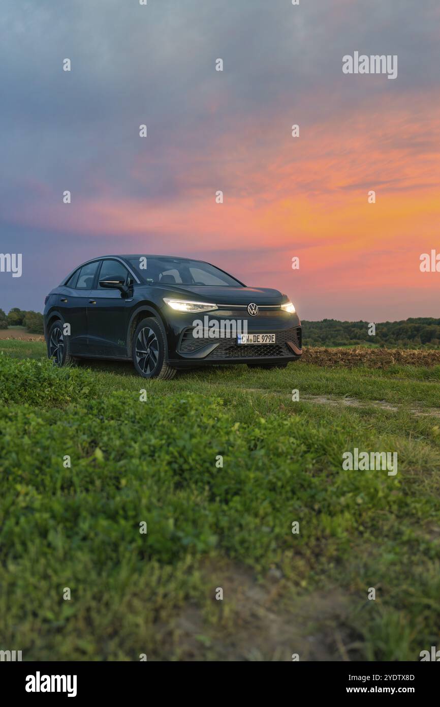 Un'auto di fronte a un impressionante cielo colorato durante il tramonto, auto elettrica, VW ID5, Gechingen, Foresta Nera, Germania, Europa Foto Stock