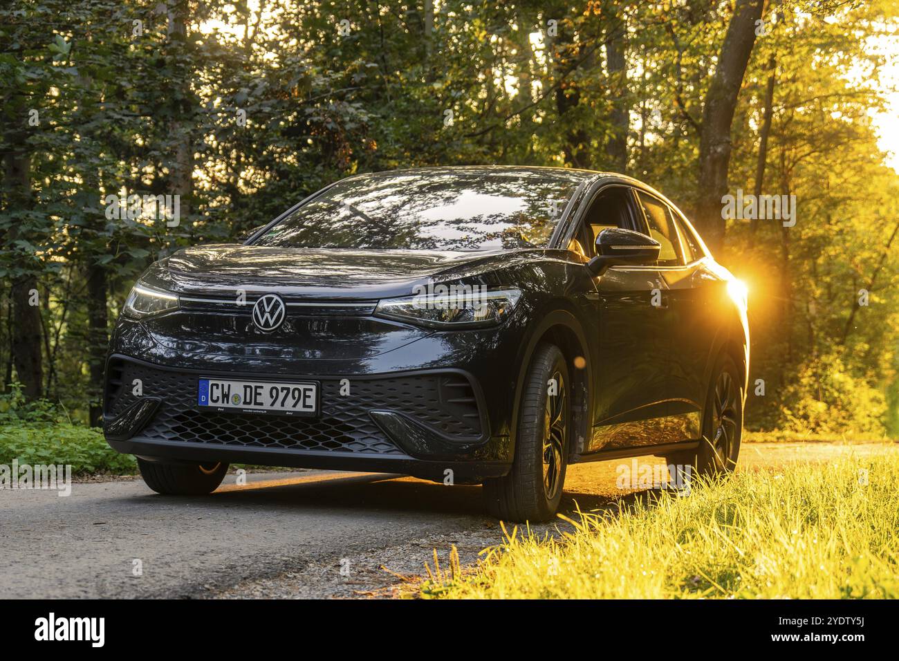 Vista frontale di un'auto su una strada nella foresta durante il tramonto, auto elettrica, VW ID5, Gechingen, Foresta Nera, Germania, Europa Foto Stock