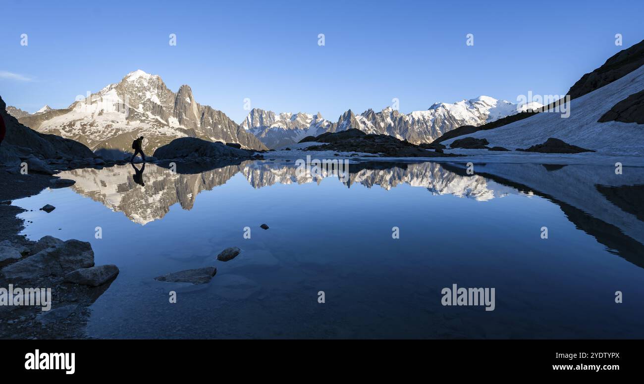 Alpinista, silhouette di fronte al paesaggio montano alla luce della sera, riflessi d'acqua nel Lac Blanc, vetta della montagna, Aiguille verte, Grandes Jor Foto Stock