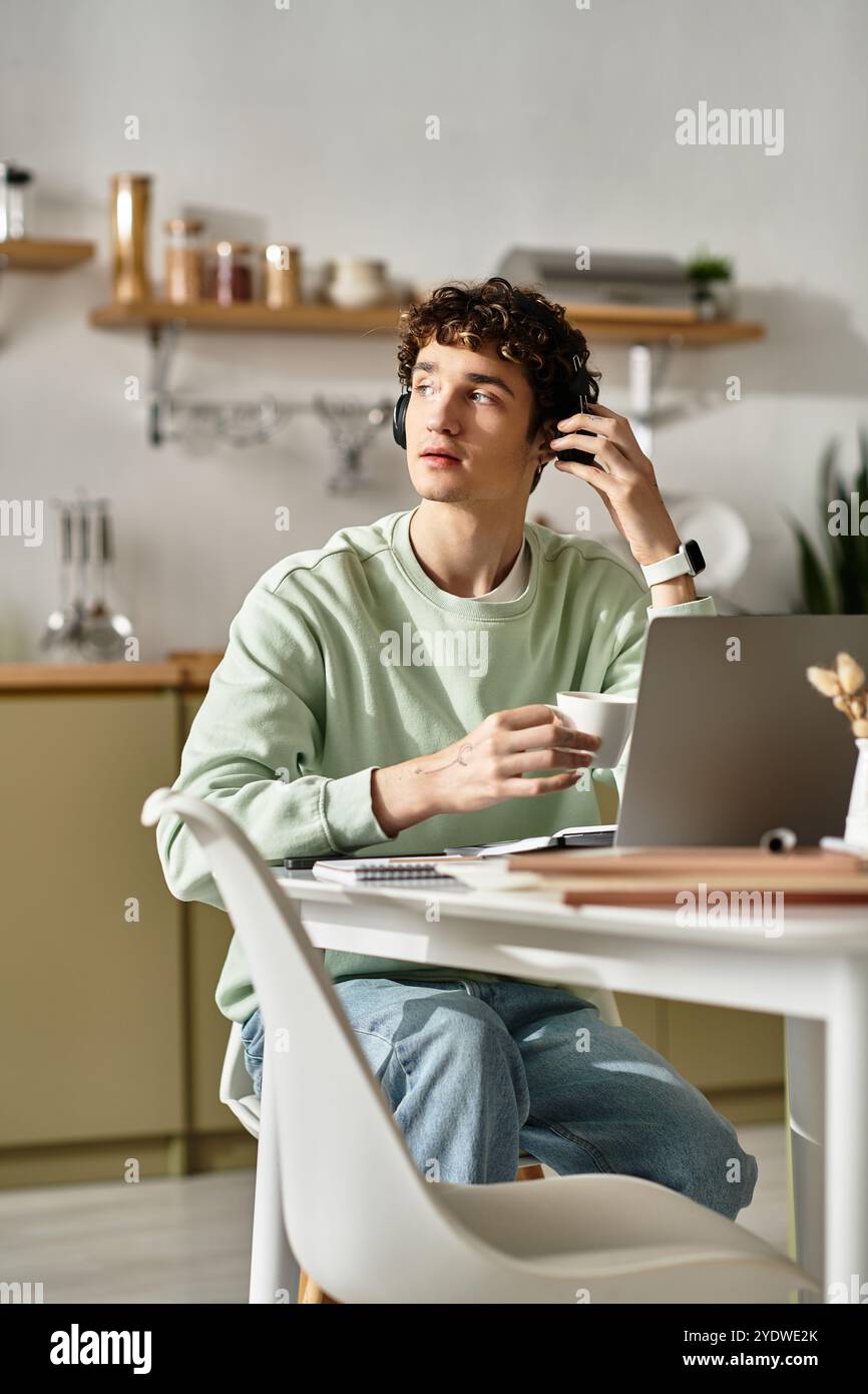 Un giovane ama il suo caffè mentre si concentra sul suo lavoro in un appartamento moderno e accogliente. Foto Stock