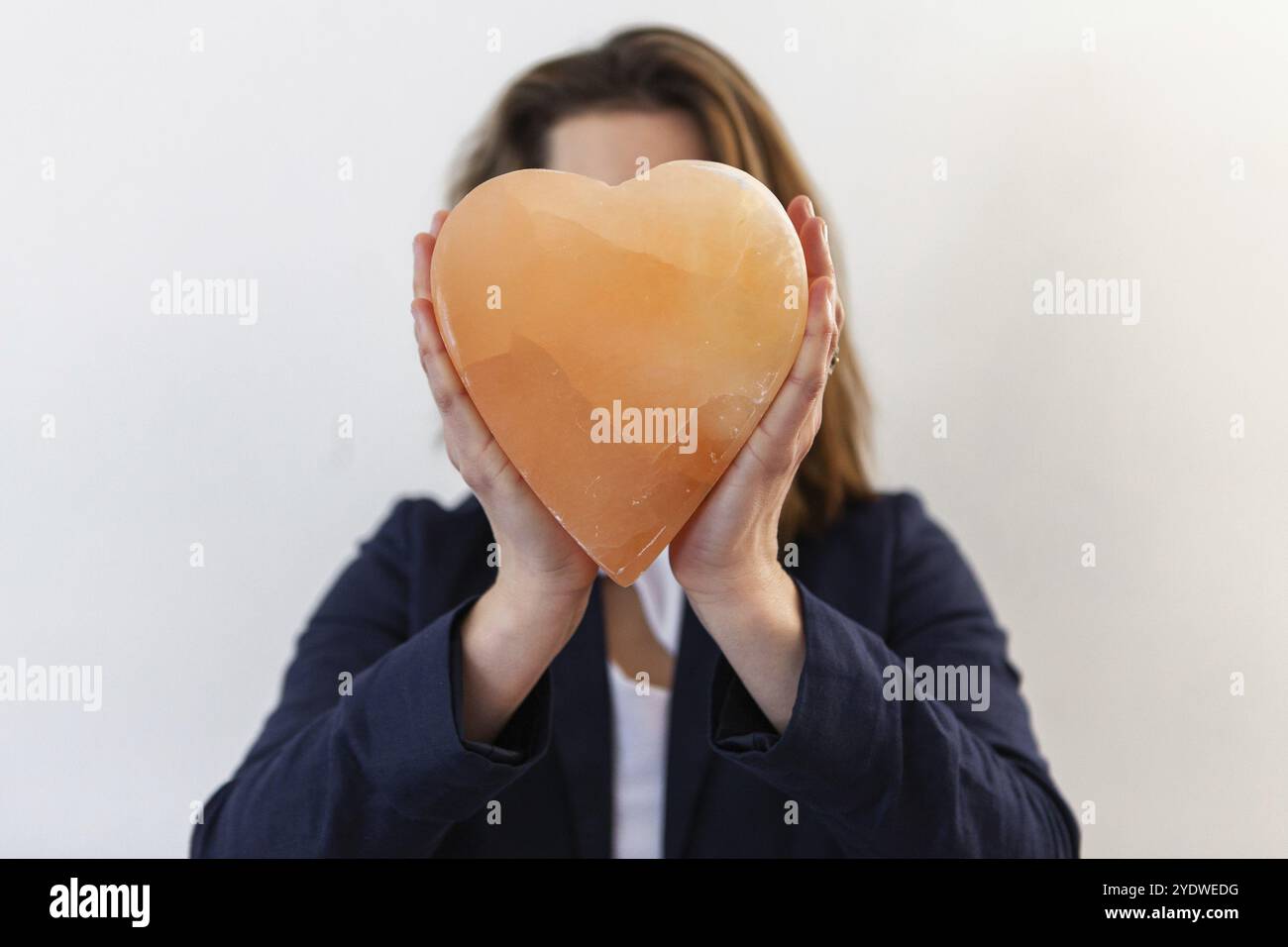 Una donna di successo viene visto dalla parte anteriore contro uno sfondo bianco, tenendo a forma di cuore in pietra minerale sul suo viso utilizzati in alternativa la salute th Foto Stock
