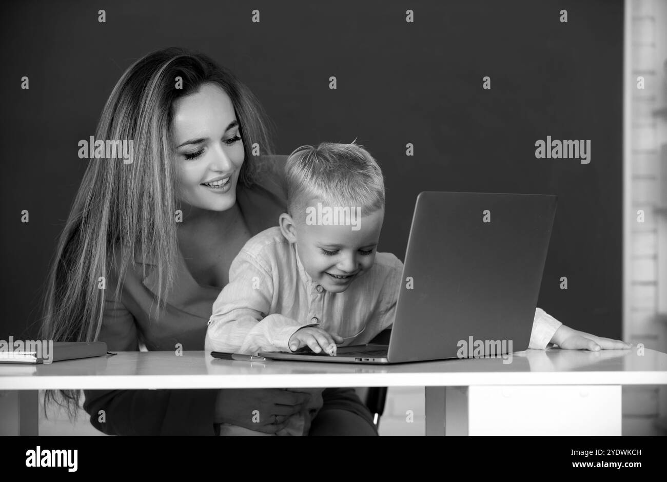 L'insegnante aiuta i bambini della scuola ad imparare la lezione, usando il laptop. Apprendimento di madre e figlio. Foto Stock