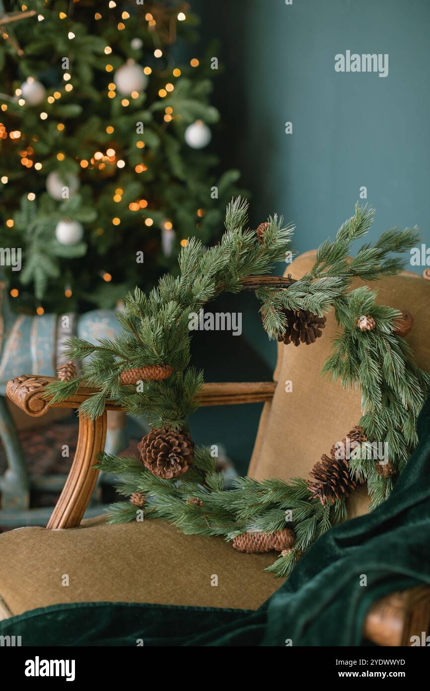 Corona di Natale rustica su una poltrona vintage di fronte a un albero di Natale illuminato in un soggiorno Foto Stock