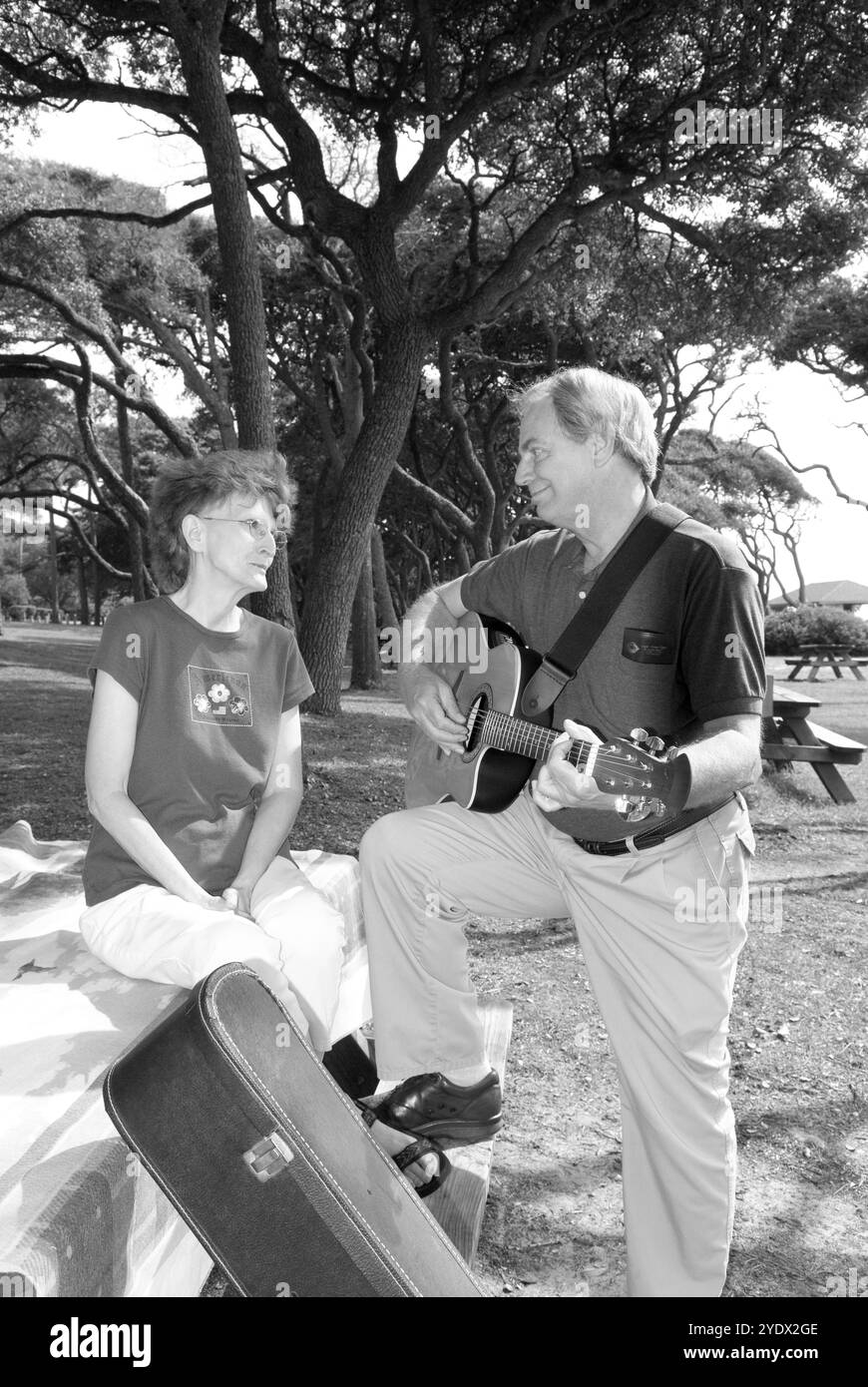 Coppia caucasica, da 50 a 55 anni, che si rilassa a un tavolo da picnic nel Myrtle Beach State Park, South Carolina, USA, con l'uomo che suona la chitarra. Foto Stock