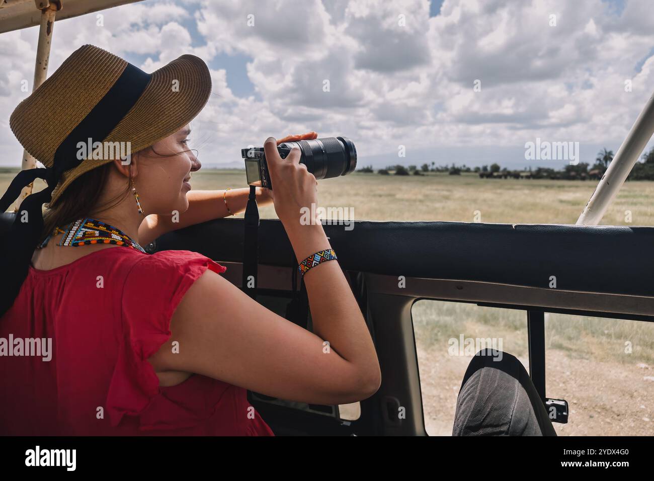 Fotografa professionista durante il safari. La donna appoggia la fotocamera su un sacco di fagioli e scatta foto alla fauna selvatica da un veicolo da safari. Nel Masai Mara, Kenya. Foto Stock
