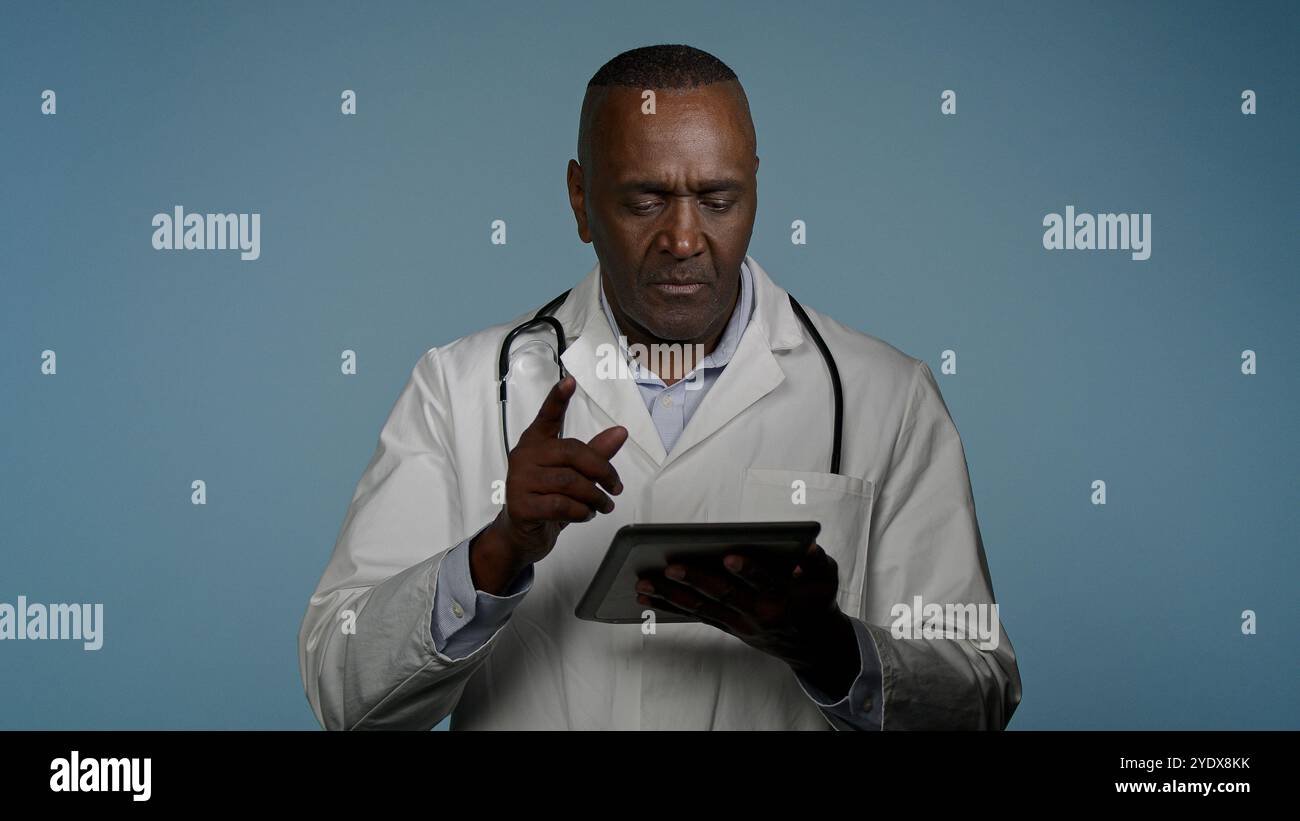 Uomo medico afroamericano uomo operatore sanitario che utilizza tablet digitale per la ricerca di laboratorio in studio blu sfondo moderno controllo di trattamento Foto Stock