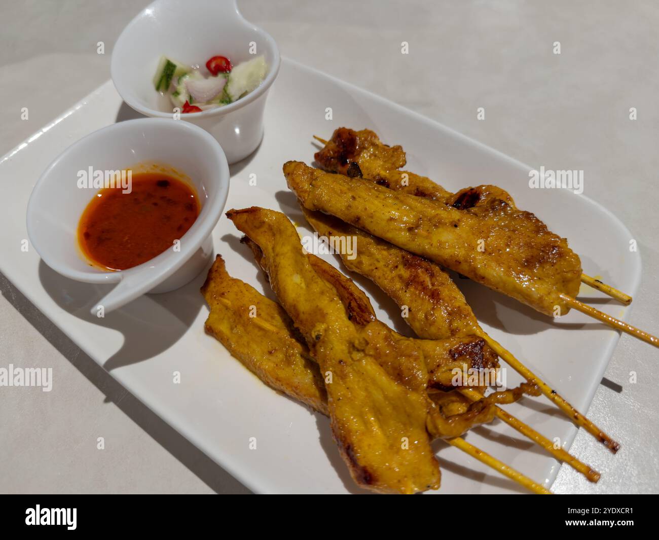 Spiedini di pollo satay alla griglia serviti con salse serviti su un lungo piatto bianco e posti su un tavolo. Cucina tailandese o asiatica. Foto Stock