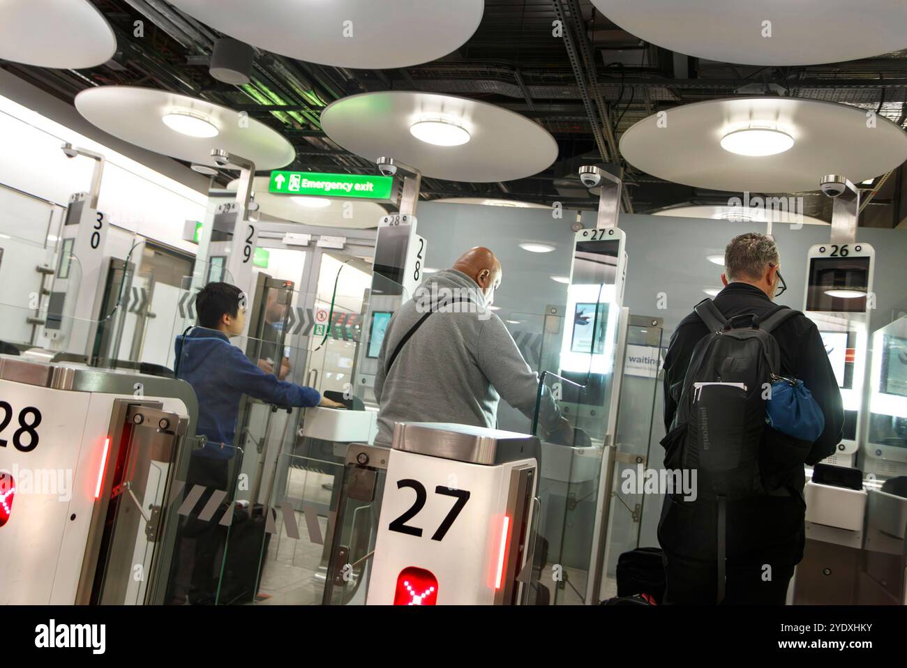 I viaggiatori che si allineano al controllo di frontiera del Regno Unito all'interno di un terminal 5 dell'aeroporto LHR heathrow con esclusive luci circolari a soffitto Foto Stock