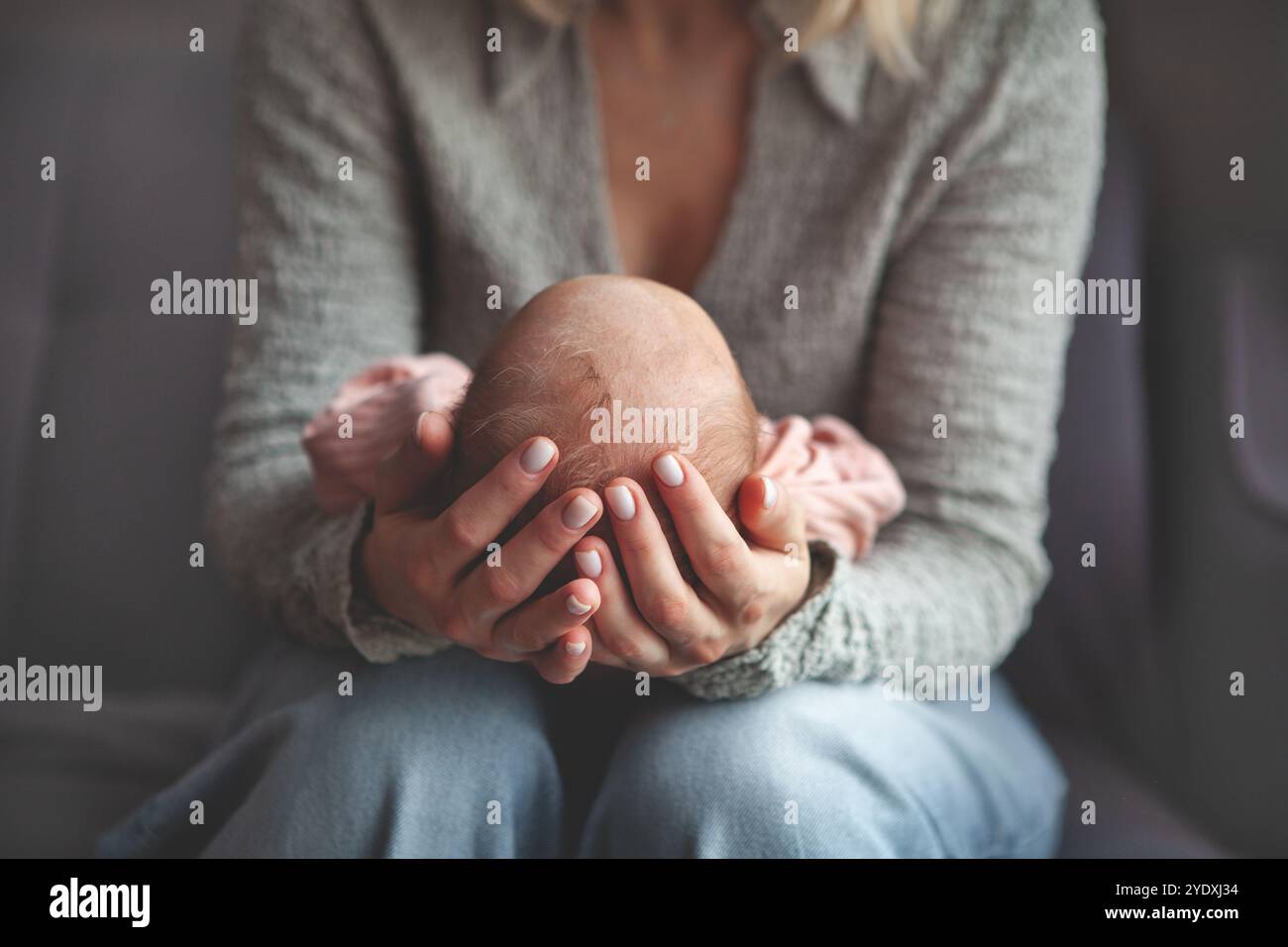 Primo piano la mamma culla e dondola delicatamente il neonato tra le braccia. Concentratevi sulle mani che tengono il bambino, catturando un momento tenero e intimo di cura materna e lov Foto Stock