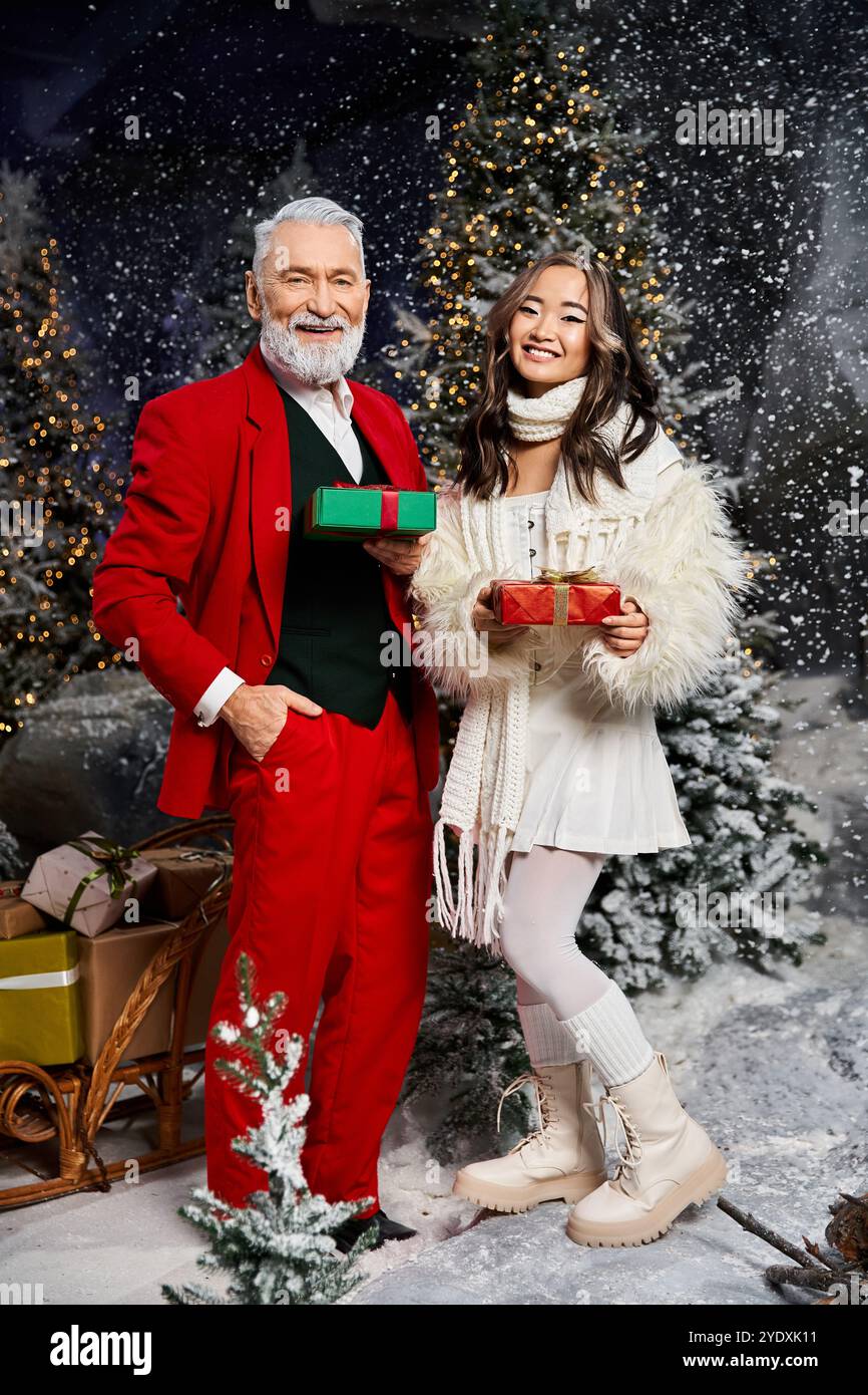 Un Babbo Natale gioioso e una donna con regali colorati festeggiano in una scena innevata e festosa. Foto Stock