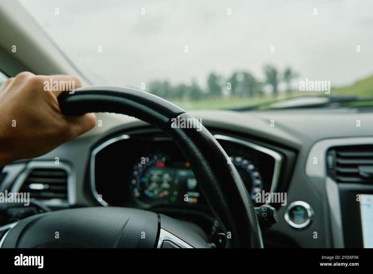 Il conducente deve afferrare il volante con una visuale della campagna davanti al parabrezza. Uomo che guida un'auto in giornata di pioggia. Vista interna del veicolo moderno Foto Stock