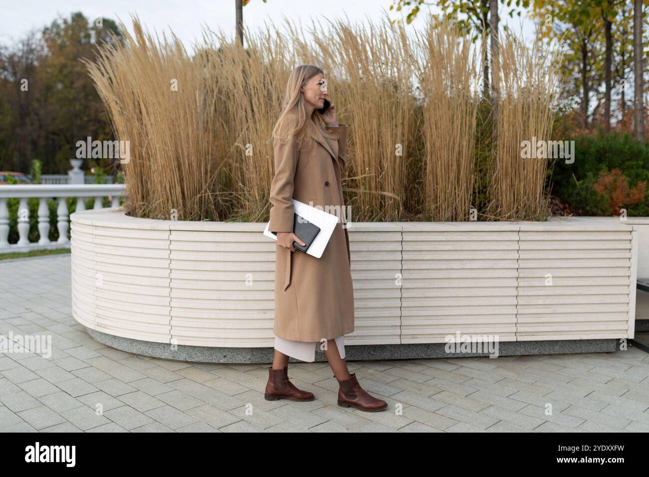 Una donna d'affari cammina vicino a un business center, tenendo un computer portatile e parlando al telefono Foto Stock