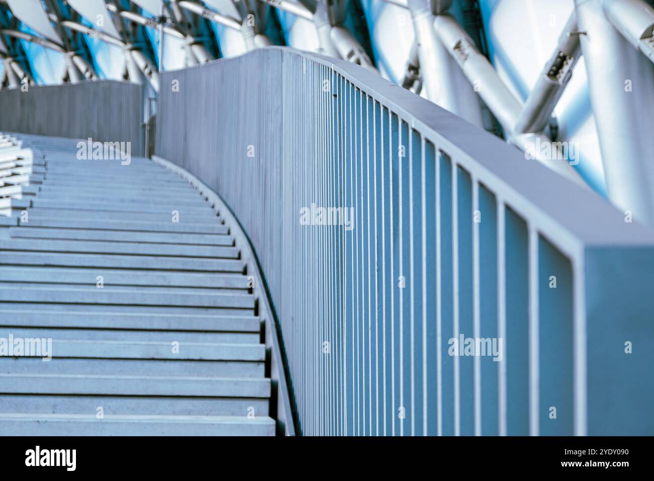 Una scala contemporanea presenta un corrimano liscio e ricurvo e gradini lineari, adagiati su uno sfondo di vibranti blu e strutture metalliche su un sunn Foto Stock