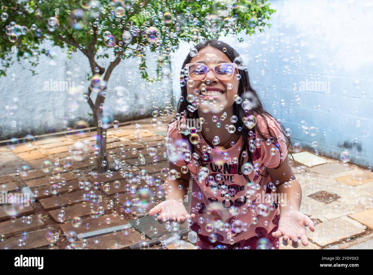 Goiania, Goias, Brasile – 13 ottobre 2024: Una ragazza che si diverte nel suo giardino e bolle di sapone intorno. Foto Stock