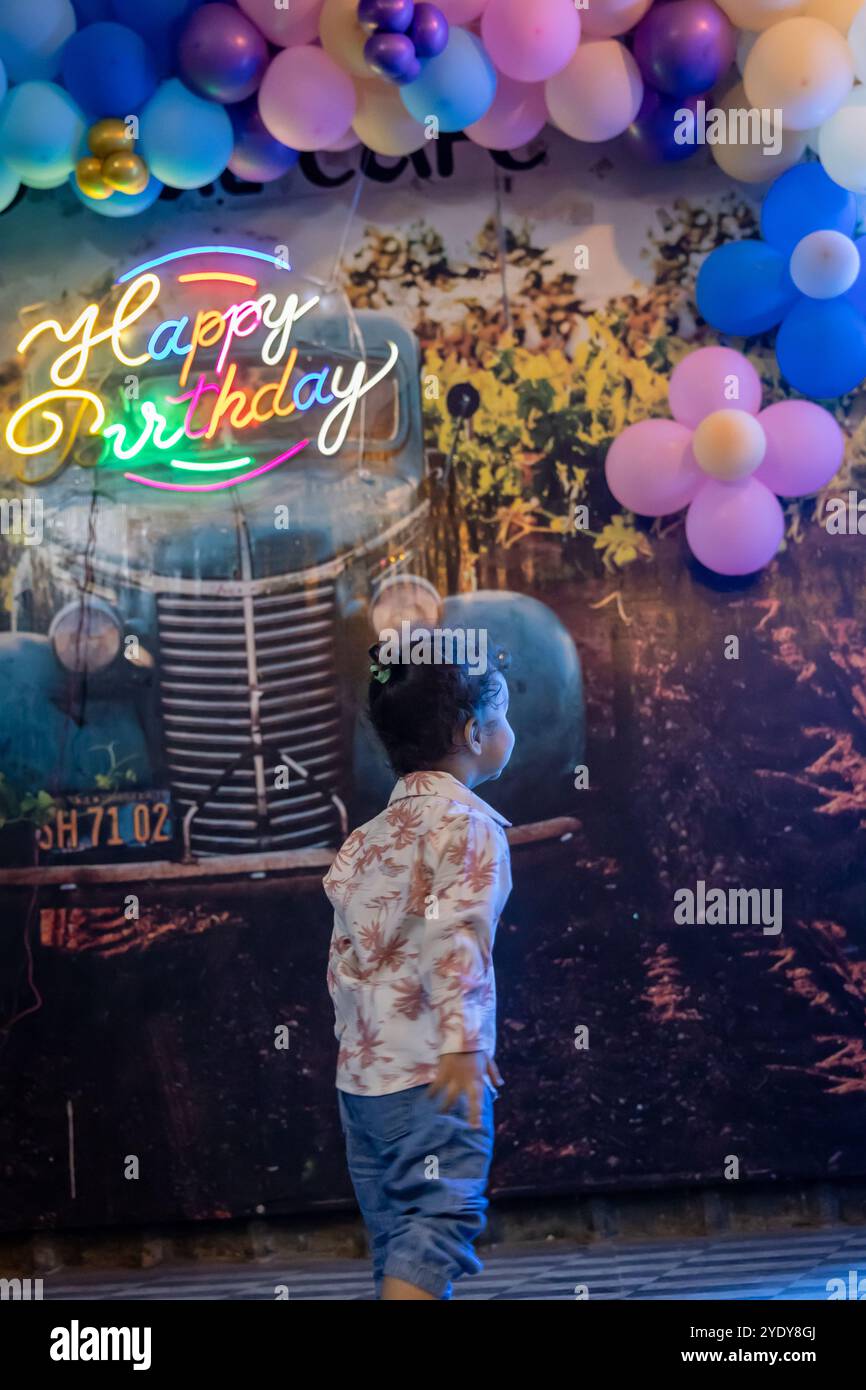 Simpatico ragazzo indiano che ammira l'arredamento e lo sfondo da un angolo piatto delle mongolfiere di compleanno Foto Stock