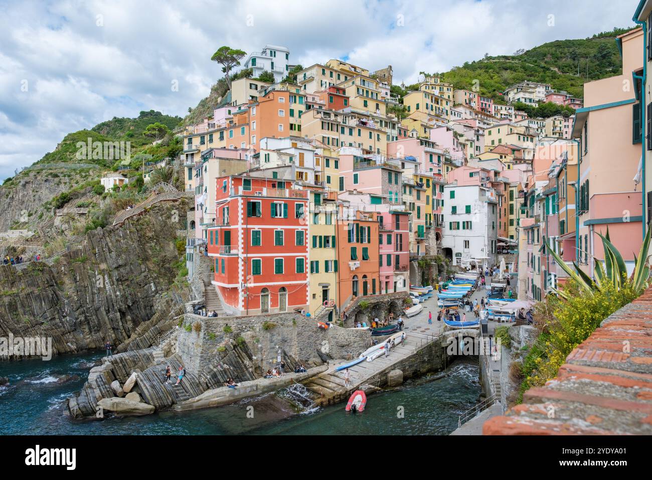 Accoccolati contro scogliere ripide, gli edifici vibranti delle cinque Terre si aggrappano precariamente alla costa, riflettendo sfumature colorate. Riomaggiore alle cinque Terre, Italia Foto Stock