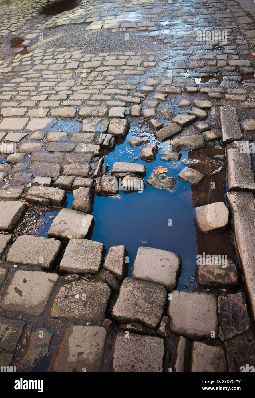 Una vecchia strada acciottolata con pietre mancanti e rotte. Foto Stock