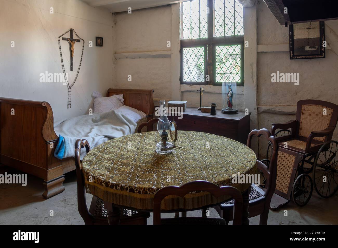 Interno di una casa del XIX secolo con letto vecchio, rosario d'epoca e sedia a rotelle d'epoca presso il museo all'aperto di Bokrijk, Limburgo, Fiandre, Belgio Foto Stock