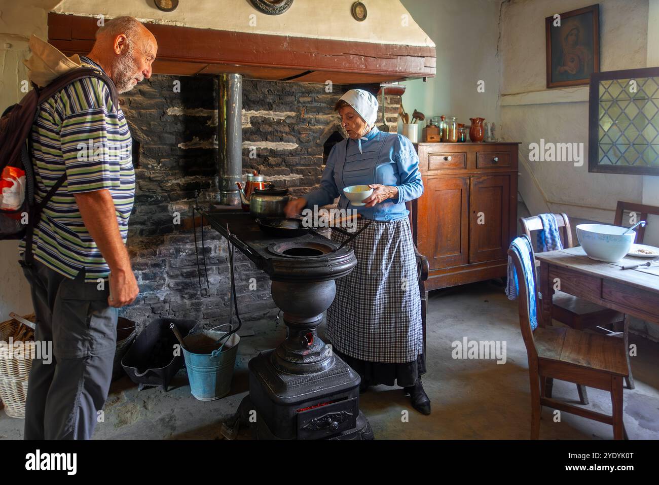 Vecchia donna che cucina su un'antica stufa a carbone fiamminga in ghisa / stoof Leuvense in casa del XIX secolo, museo all'aperto Bokrijk, Limburgo, Fiandre, Belgio Foto Stock