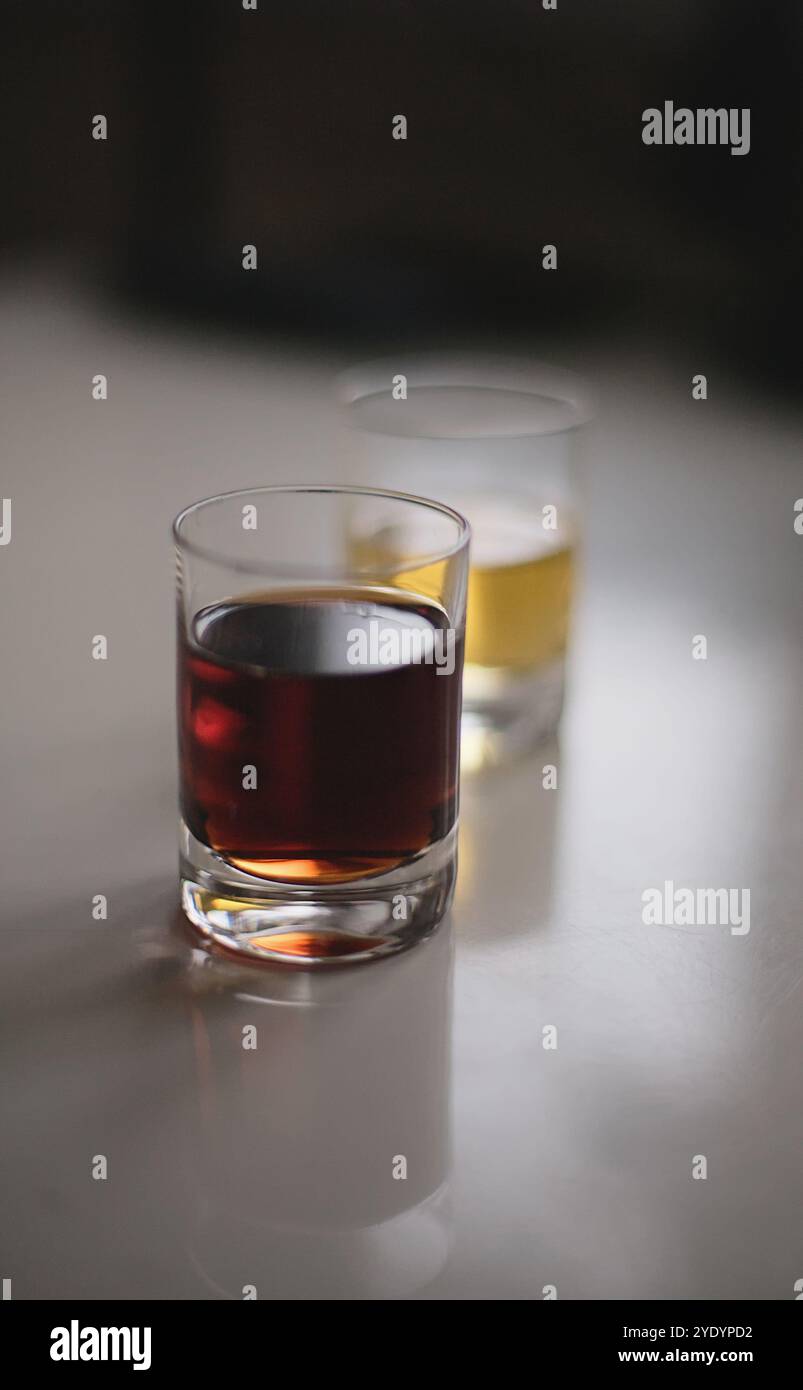 Due bicchieri da shot ripieni di bevande alcoliche rosse e gialle retroilluminate su un tavolo bianco lucido Foto Stock