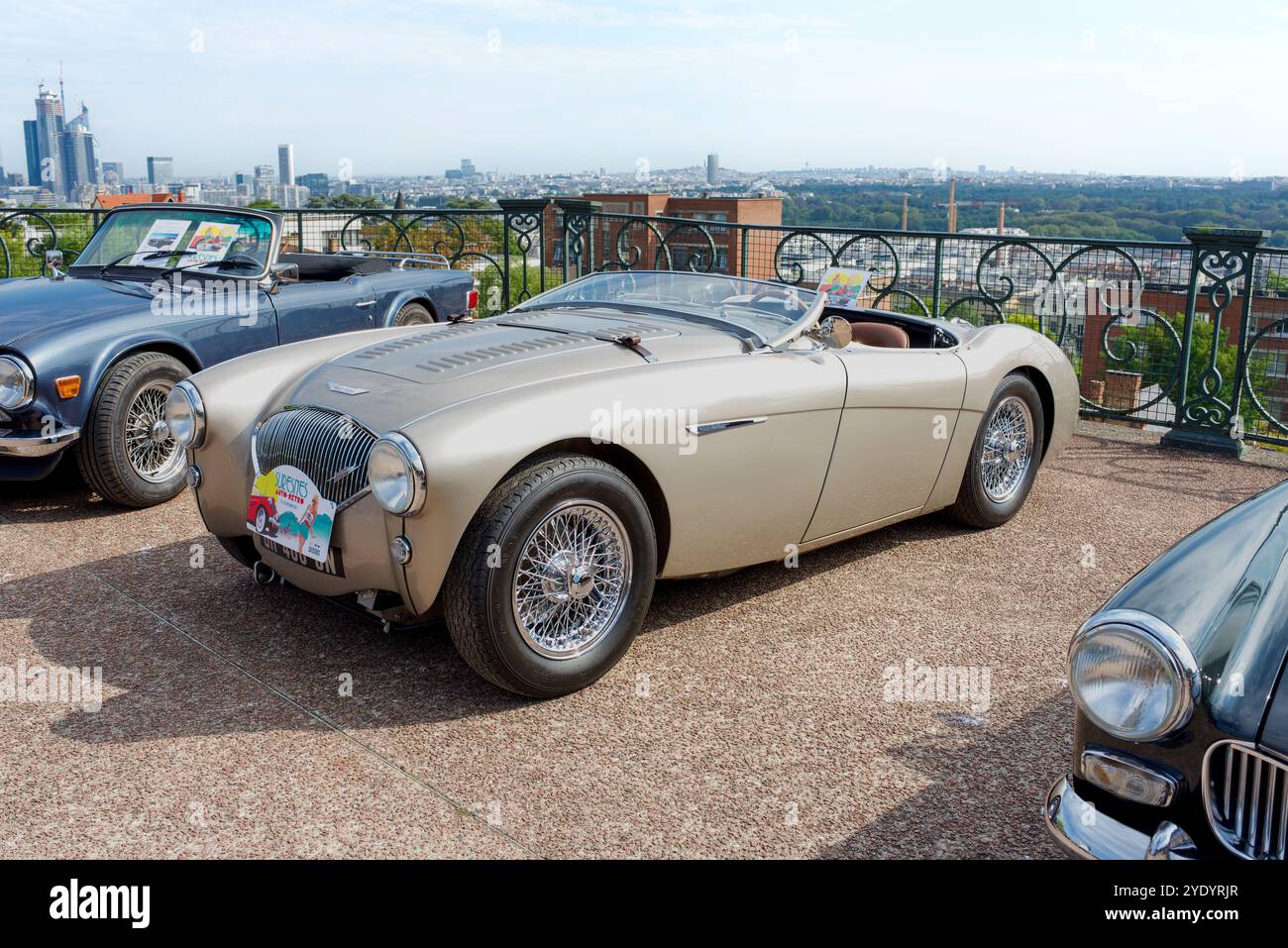 Suresnes, Francia 09.21.2024. Un'auto Austin Healey 100 ad una mostra di auto d'epoca all'aperto vicino a Parigi. Sullo sfondo Parigi e la Défense Foto Stock