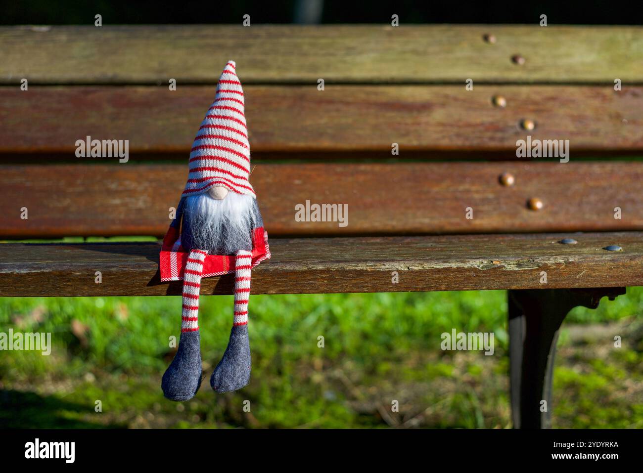Uno gnomo natalizio seduto su una panchina di legno nel parco in una soleggiata giornata autunnale. Copia spazio Foto Stock