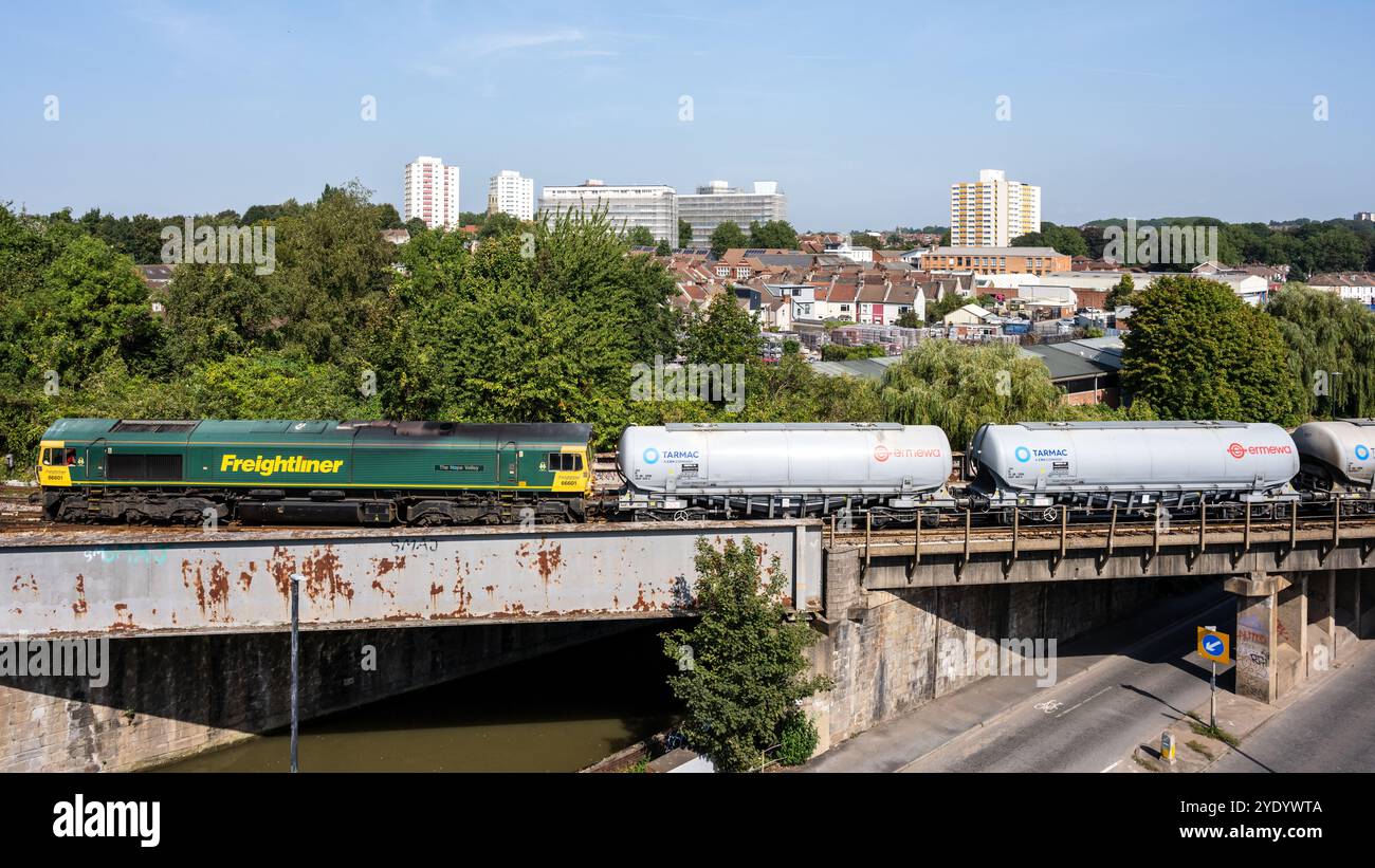 Una locomotiva Freightliner classe 66 trasporta camion cisterna Tarmac sulla Great Western Main Line a St Philip's Marsh a Bristol, con il cit residenziale Foto Stock