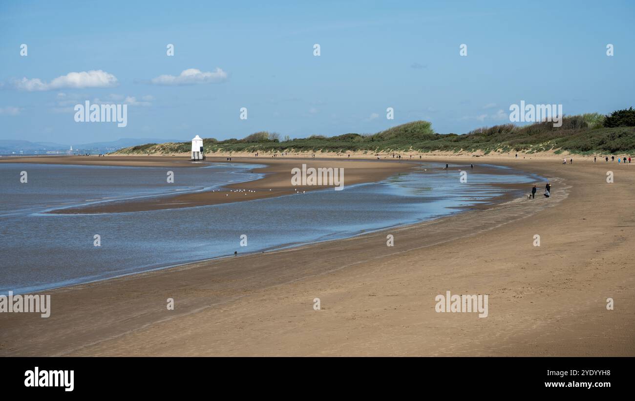 Le persone camminano davanti al faro di basso livello sulla spiaggia sabbiosa di Burnham-on-Sea sulla costa del Canale di Bristol. Foto Stock