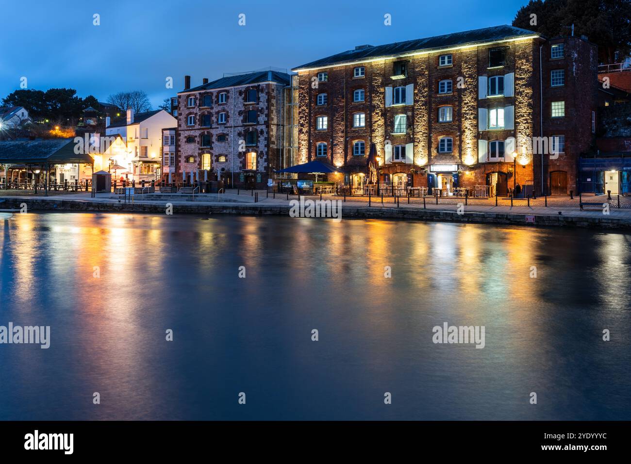 I magazzini convertiti sono illuminati di notte al molo rigenerato di Exeter sulle rive del fiume exe. Foto Stock