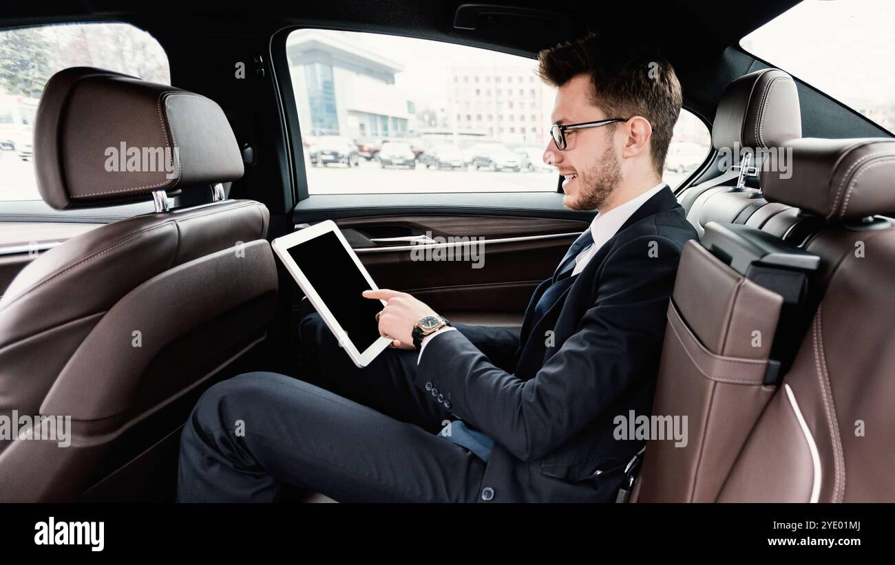 Giovane uomo d'affari che usa il suo tablet digitale in auto di lusso Foto Stock