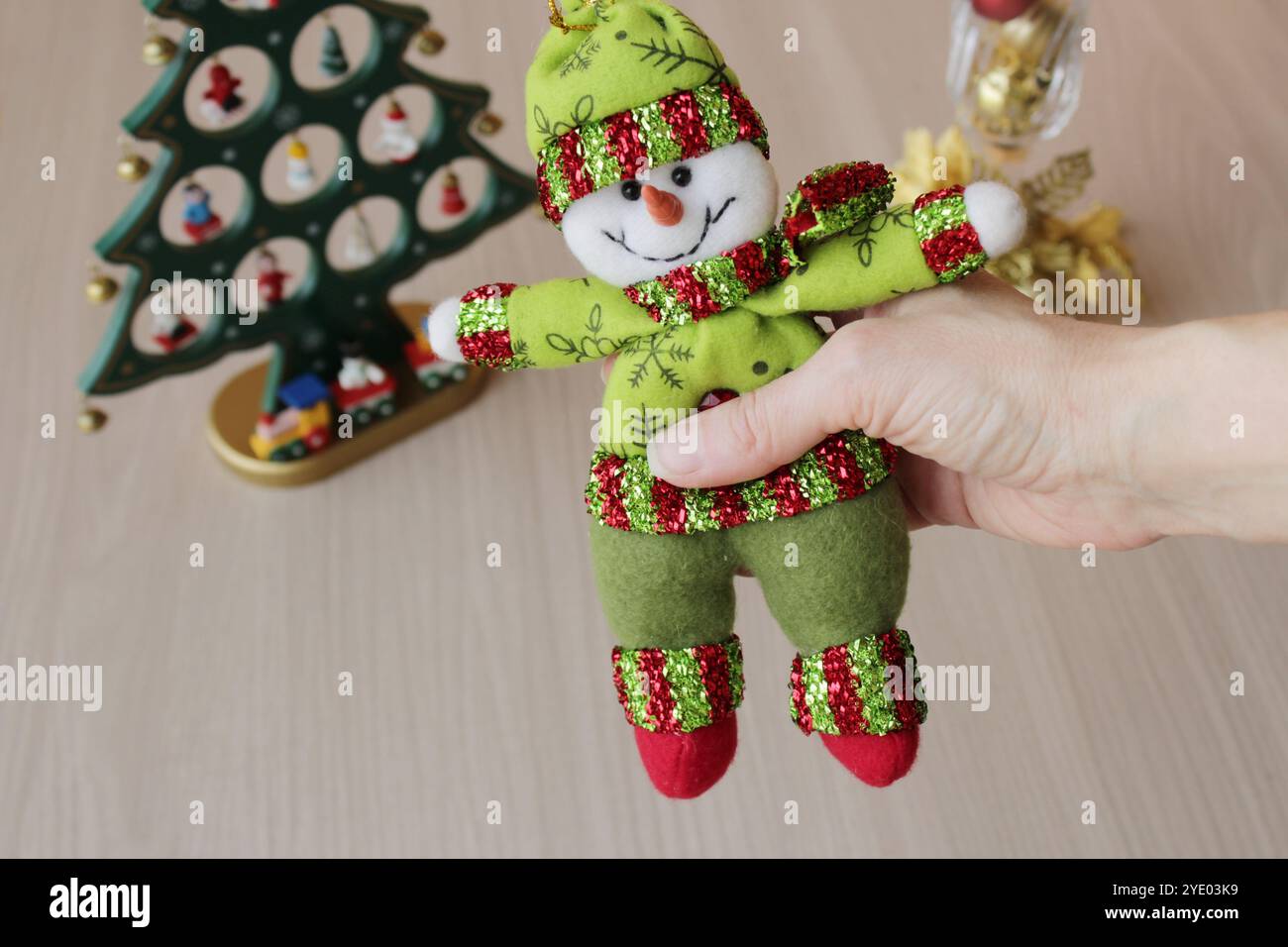 Divertente allegro pupazzo di neve imbottito in un intimo vestito verde tenuto da mano umana. Bambola artigianale per decorazioni natalizie. Dicembre stagione invernale vacanze natalizie. Foto Stock