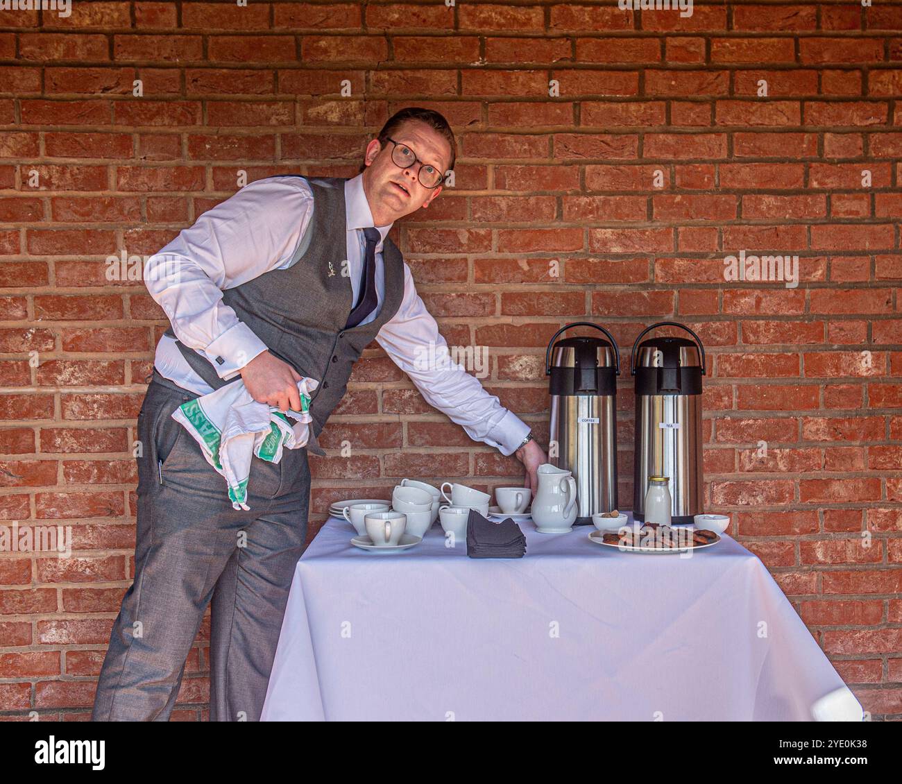 cameriere maschile che serve caffè e pasticcini in un giardino recintato Foto Stock