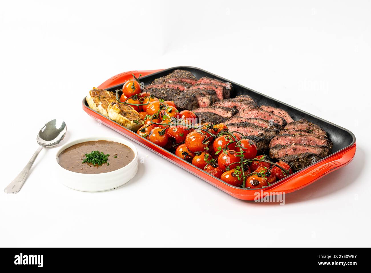 Bistecca di lombo grigliata in un piatto da forno rosso con pomodori ciliegini arrostiti e aglio. Foto Stock