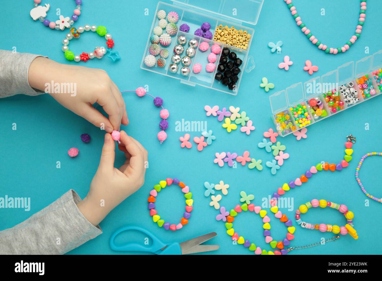 La bambina ha fatto braccialetti su sfondo blu. Gioielli con perline fatti a mano per bambini. Collane e bracciali realizzati con perle e perle multicolore. Brac. Fai da te Foto Stock