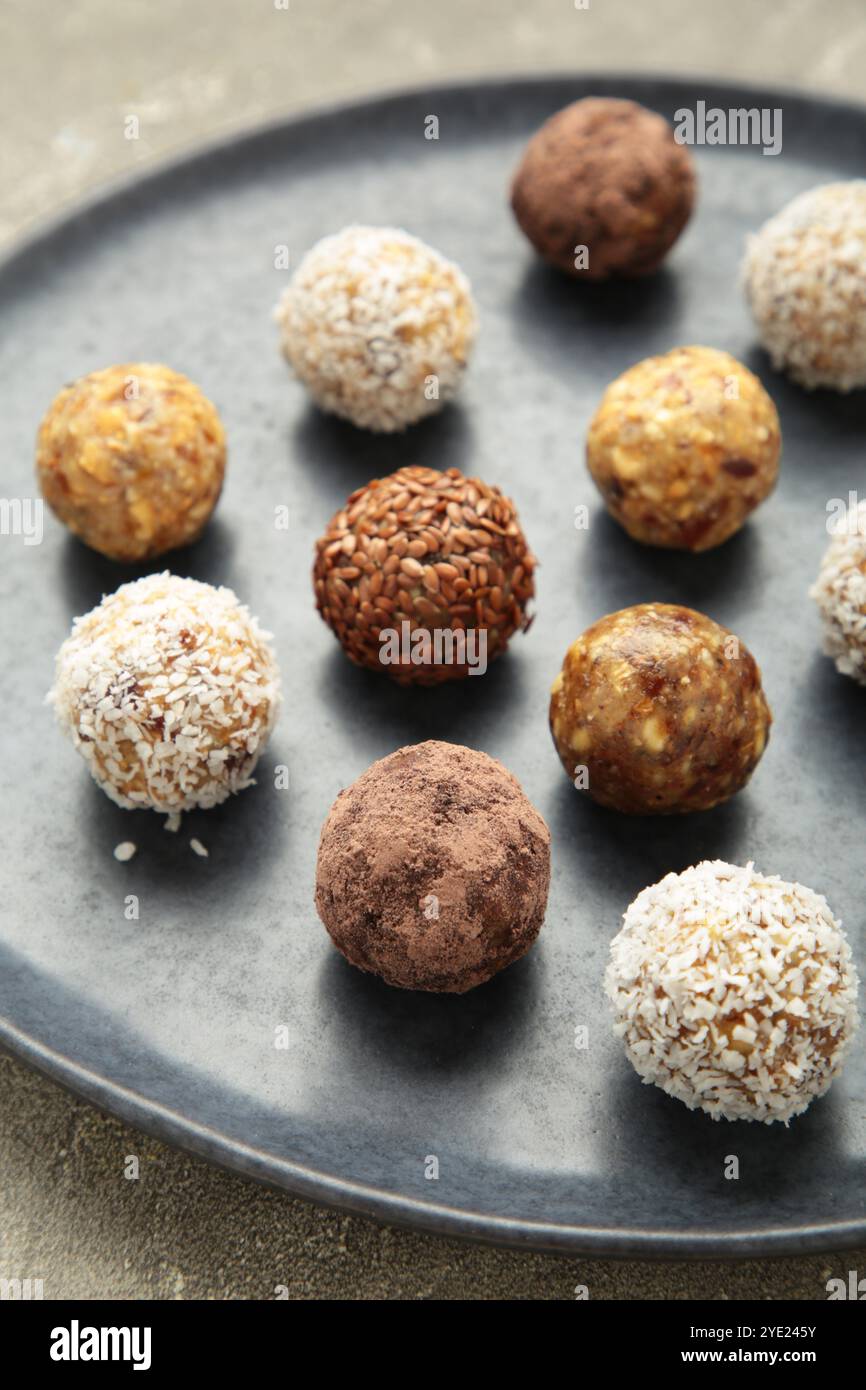 Palle di energia grezza sane. Palline vegane caramellate di datteri, noci e cocco su piatto su sfondo grigio. Vista dall'alto, concetto di caramelle fatte in casa con Foto Stock