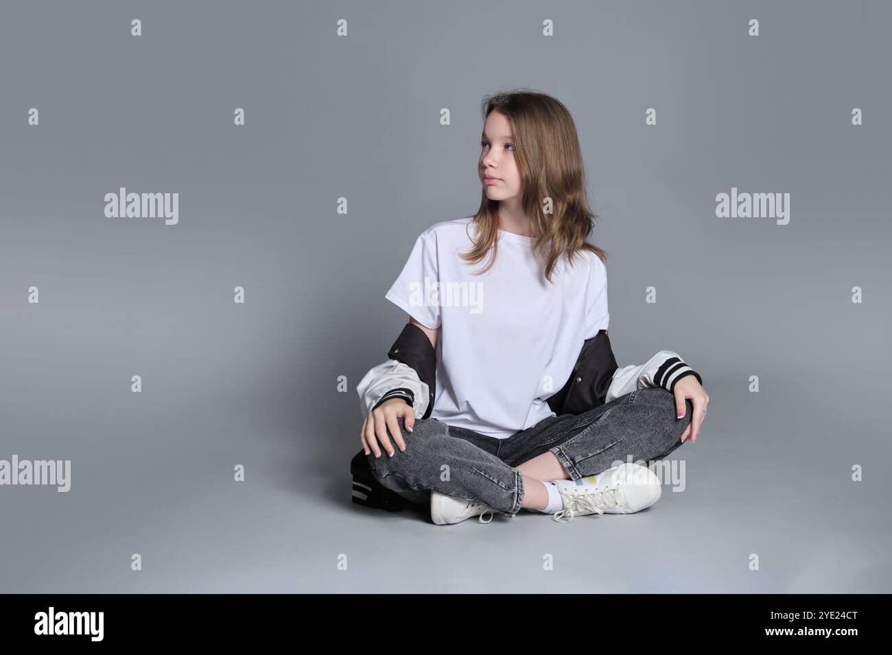 Una ragazza con un outfit casual si siede a gambe incrociate, perduta nel pensiero. Questa immagine mette in evidenza la combinazione di innocenza e maturità emergente, simboleggiando il Foto Stock