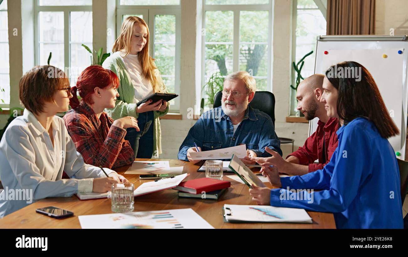 Team di professionisti diversi che discutono strategie per il tavolo da conferenza in un ufficio moderno e ben illuminato. Moderna dinamica dell'ambiente di lavoro. Foto Stock