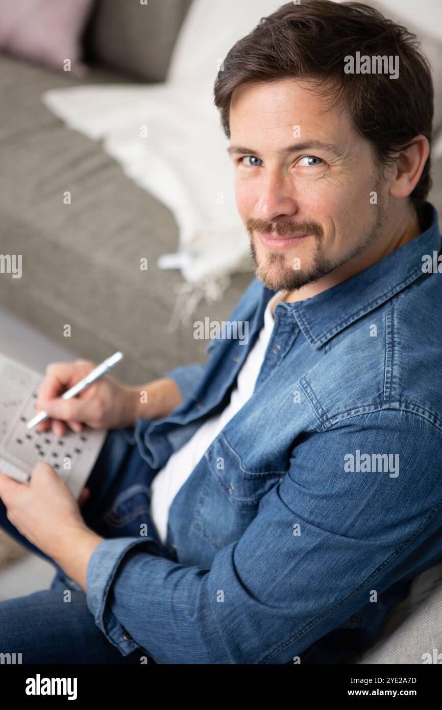 giovane uomo seduto facendo un puzzle crossword Foto Stock