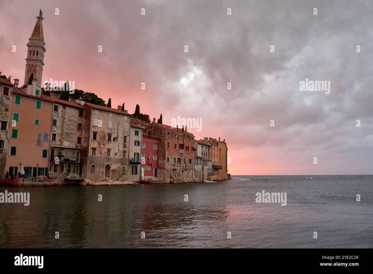 Case sul mare di Rovigno, Istria, immerse nelle calde tonalità rosse di un tramonto mozzafiato. L'iconica architettura costiera riflette la calma Foto Stock