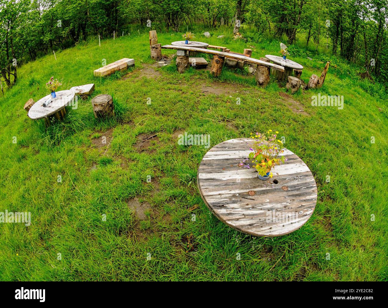 In un ambiente verde sereno, tavoli e panchine in legno rustici invitano al relax e alla conversazione, adornati da colorate composizioni floreali. Foto Stock