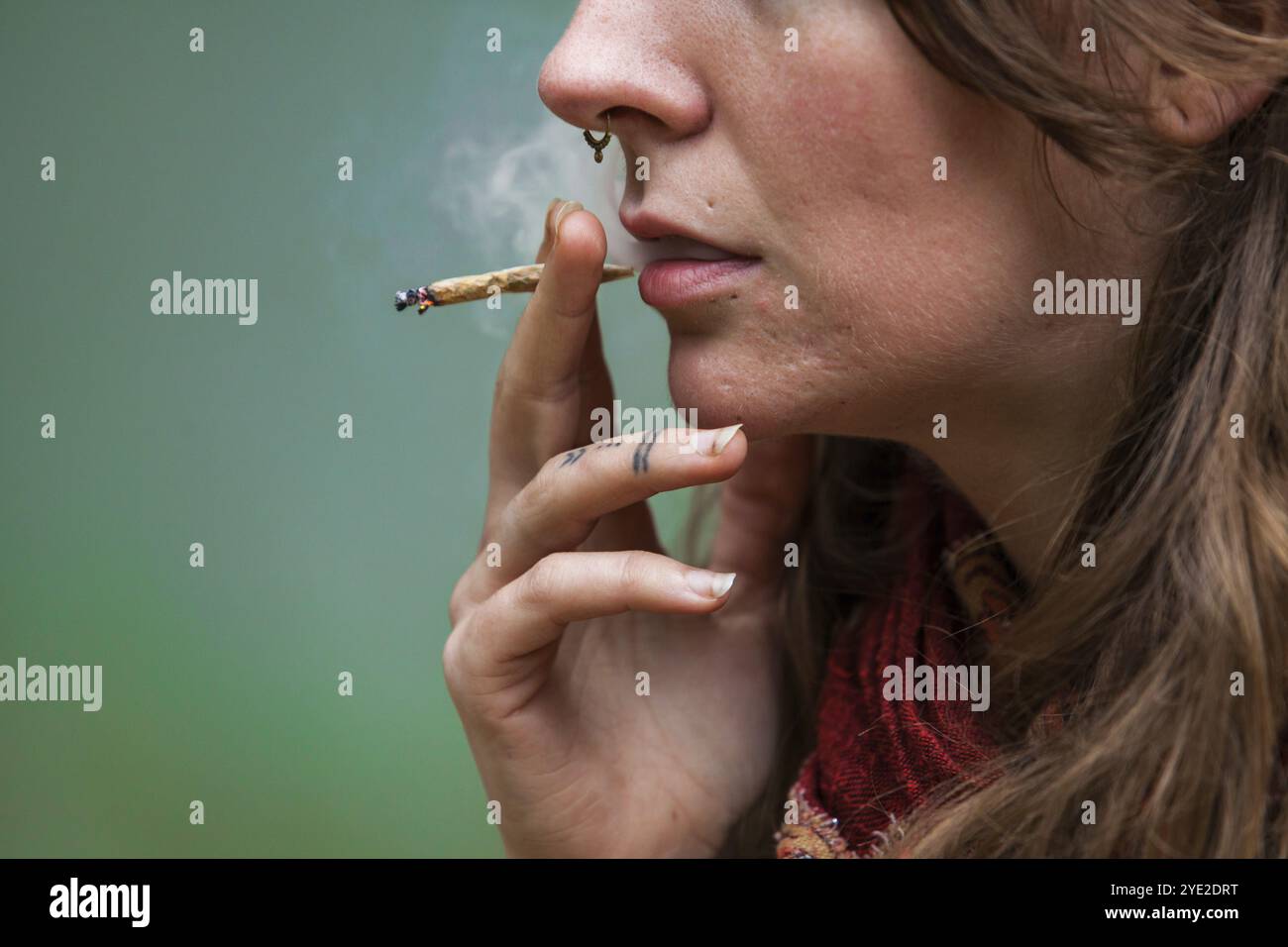 Closeup taglio corto di metà inferiore del viso della donna caucasica fumo mano rotolato marijuana comune. Sigaretta di cannabis fumata all'aperto da donna edgy Foto Stock