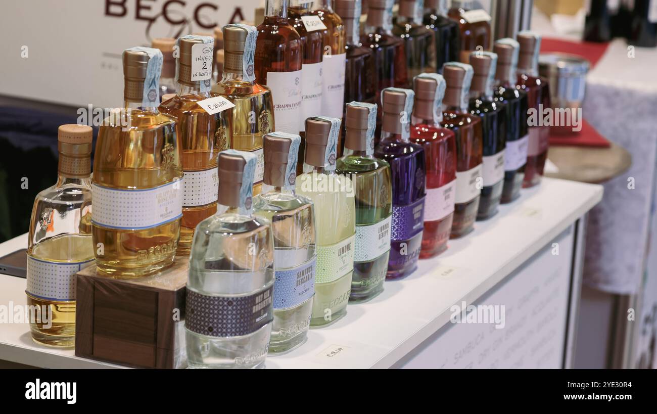 I partecipanti esplorano una vasta gamma di bottiglie colorate di liquori esposti al Festival del Tartufo d'Alba in Italia, celebrando i sapori locali Foto Stock