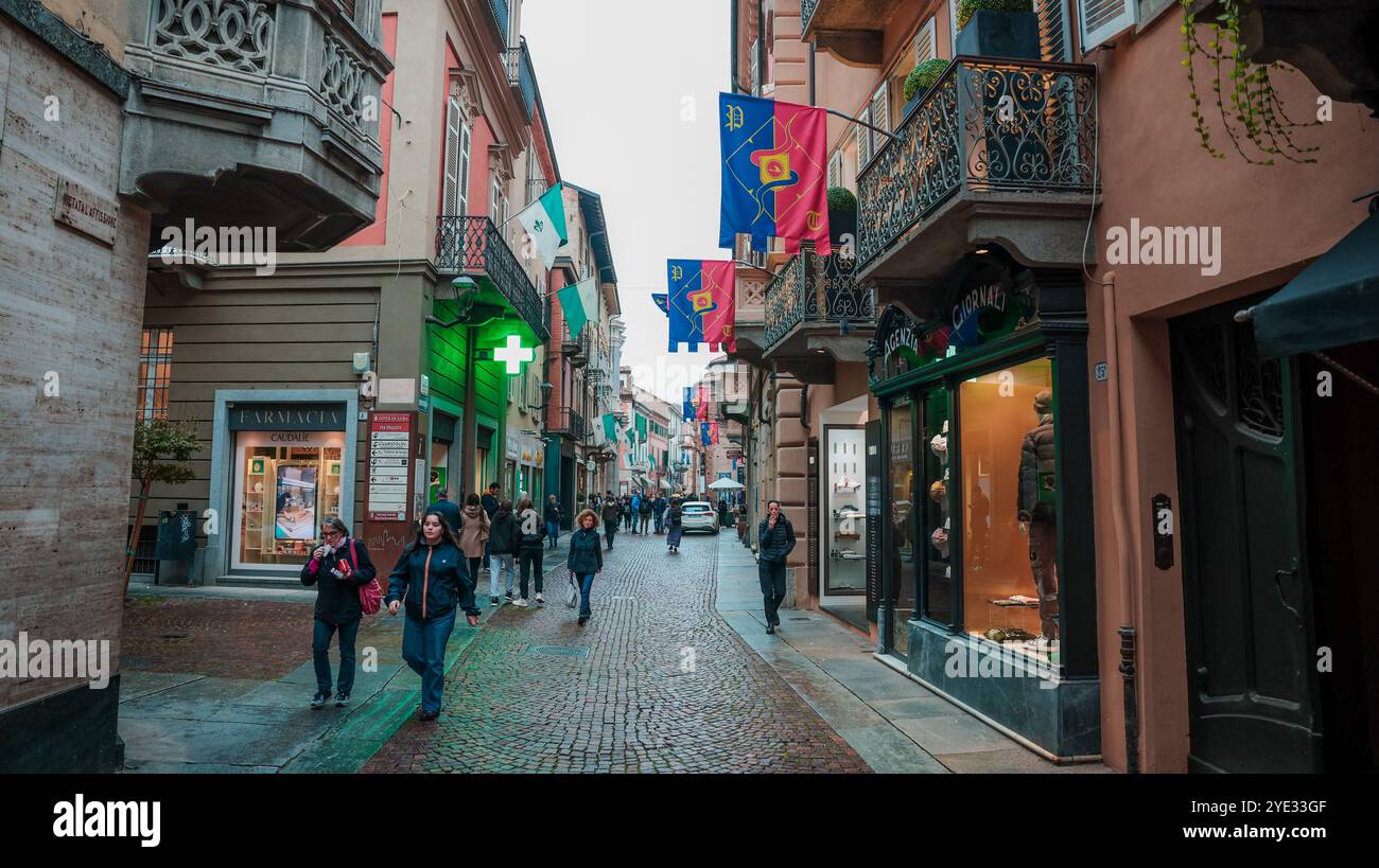 Una strada vivace ad Alba in Italia adornata da bandiere colorate. La gente passeggia attraverso il sentiero acciottolato, godendosi i negozi locali e l'atmosfera vivace Foto Stock